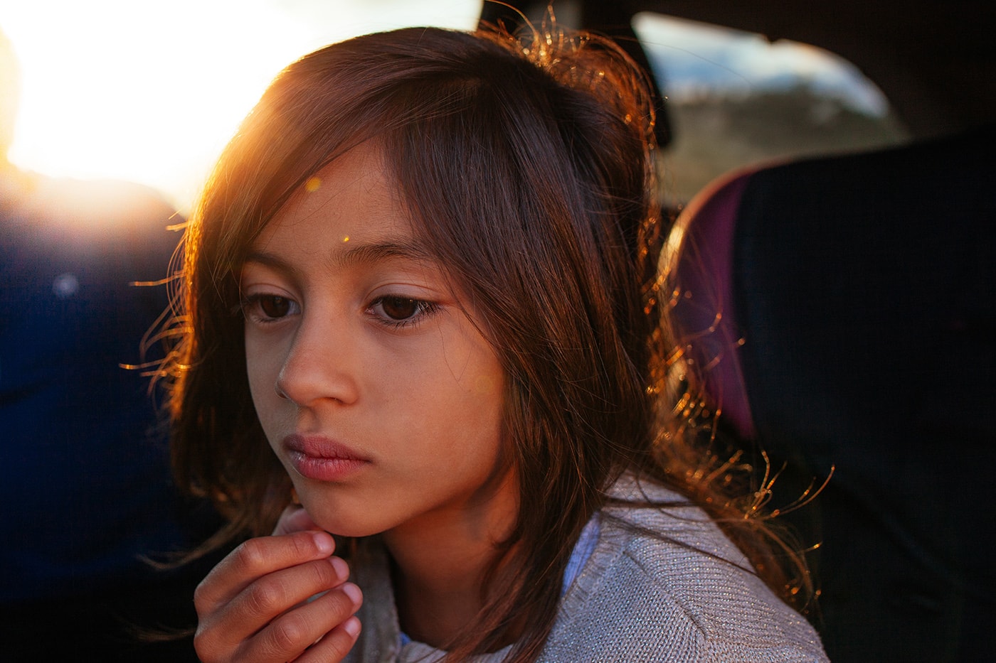 A portrait of a young girl staring off camera with her hand touching her chin.