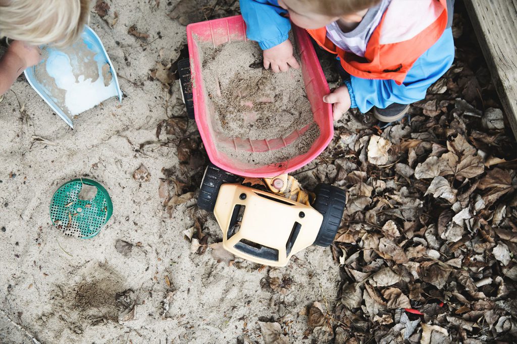 A boy and a Girl playing with shovels and trucks in the sand