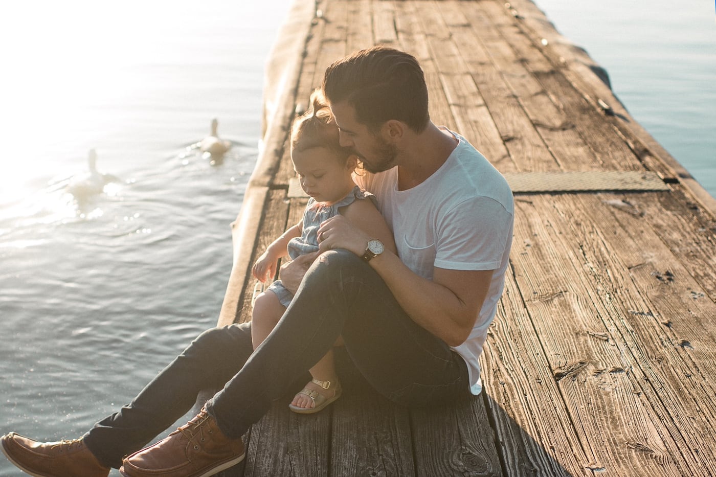Father sitting with his toddler daughter on dock on the water.