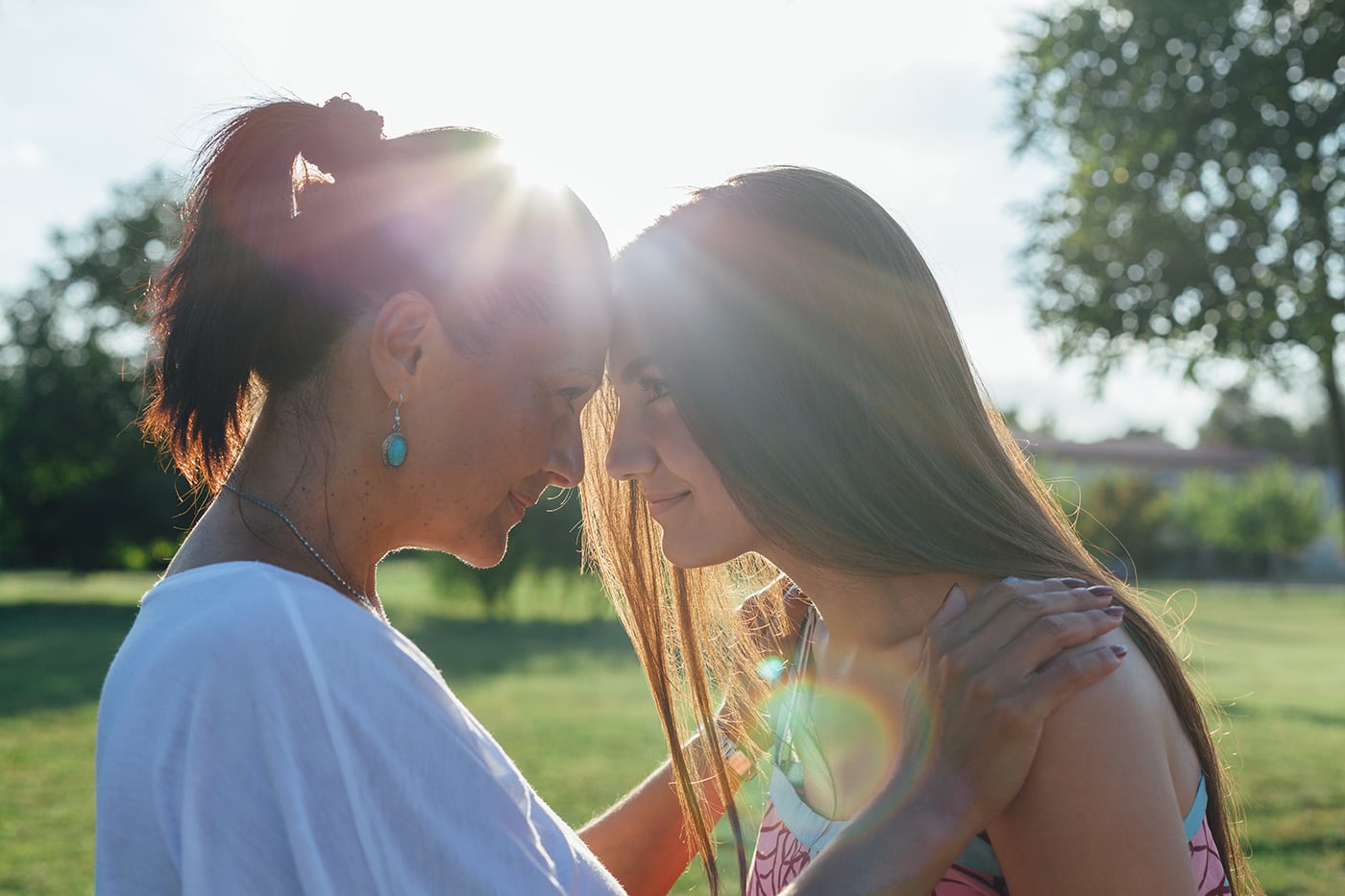 Mother and teenage daughter with foreheads together looking at each other hugging at sunset.
