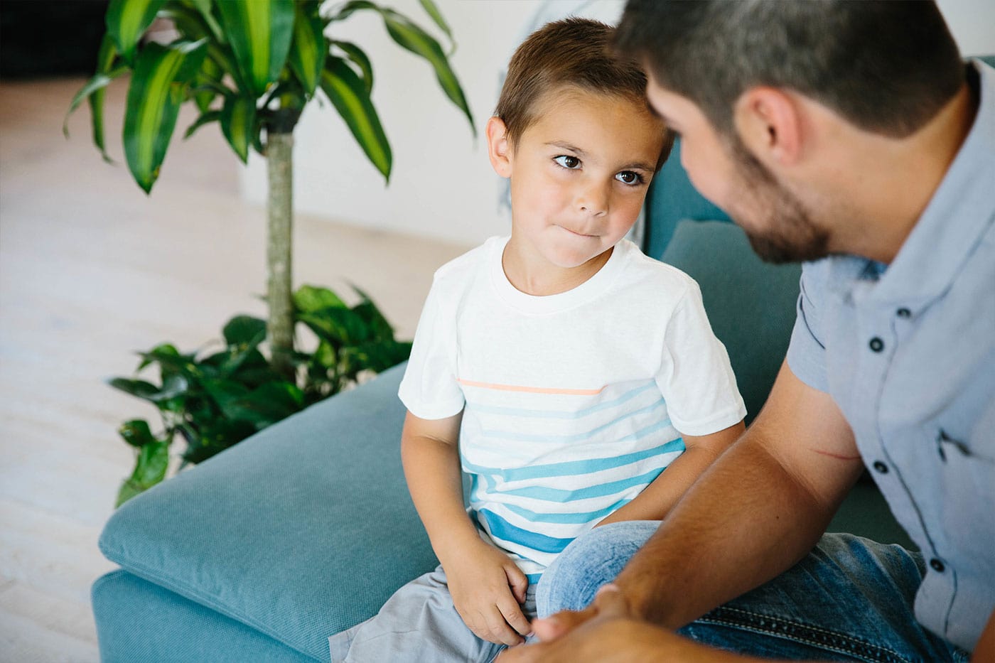 Father and son sitting on the sofa talking. The son has a mischievous look on his face but looking intently at his father.