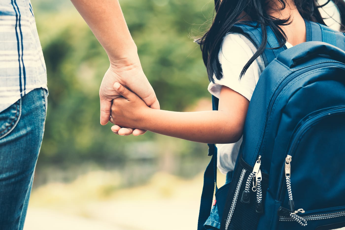 Mother holding hand of young daughter while walking to school or bus with backpack on